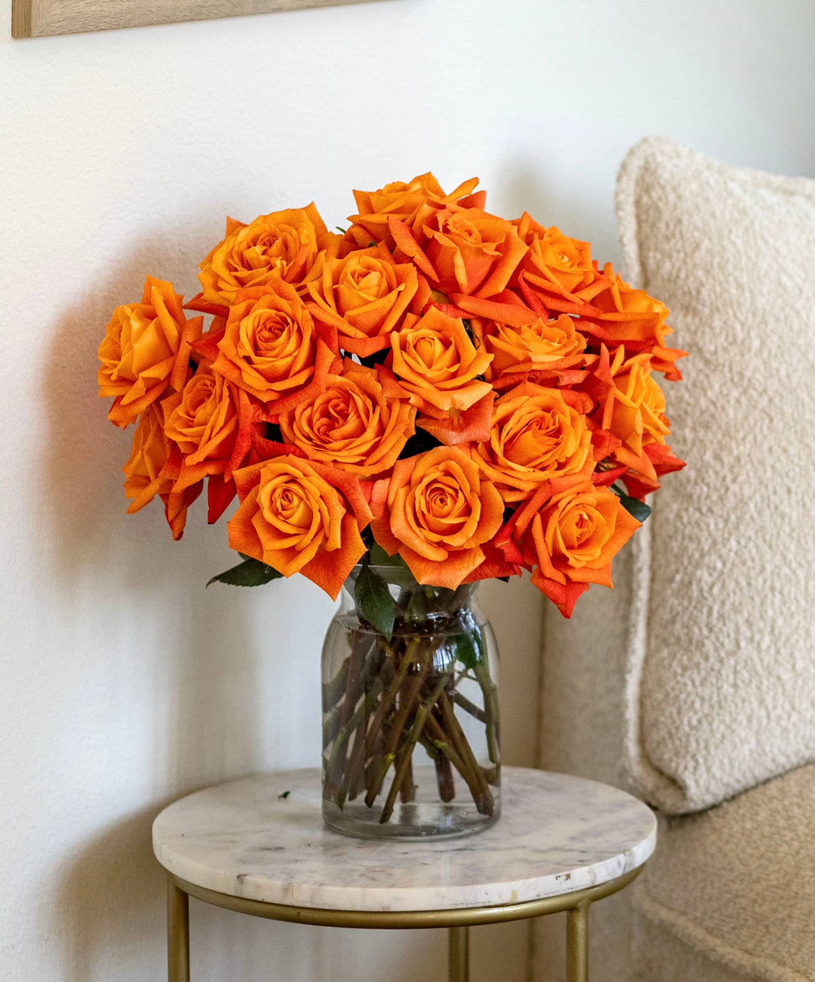 Vibrant orange rose bouquet elegantly displayed in a glass vase on a marble table.
