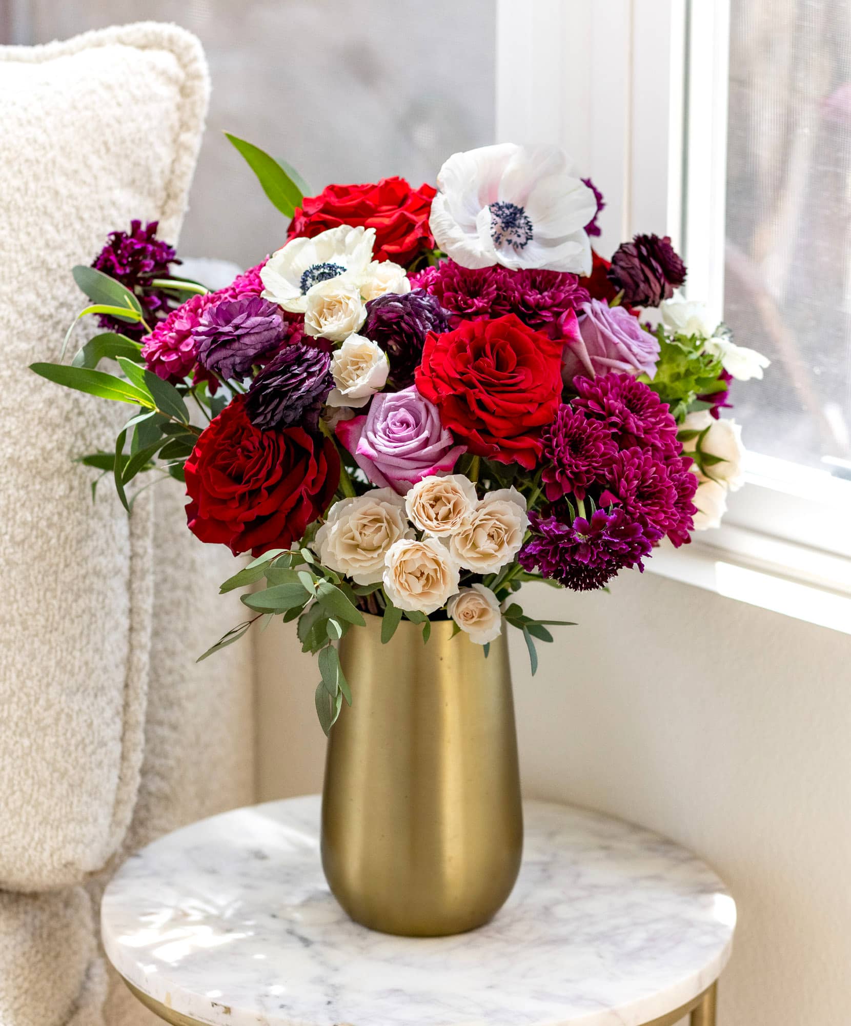Vibrant bouquet with red roses, white anemones, and purple blooms in a stylish vase.